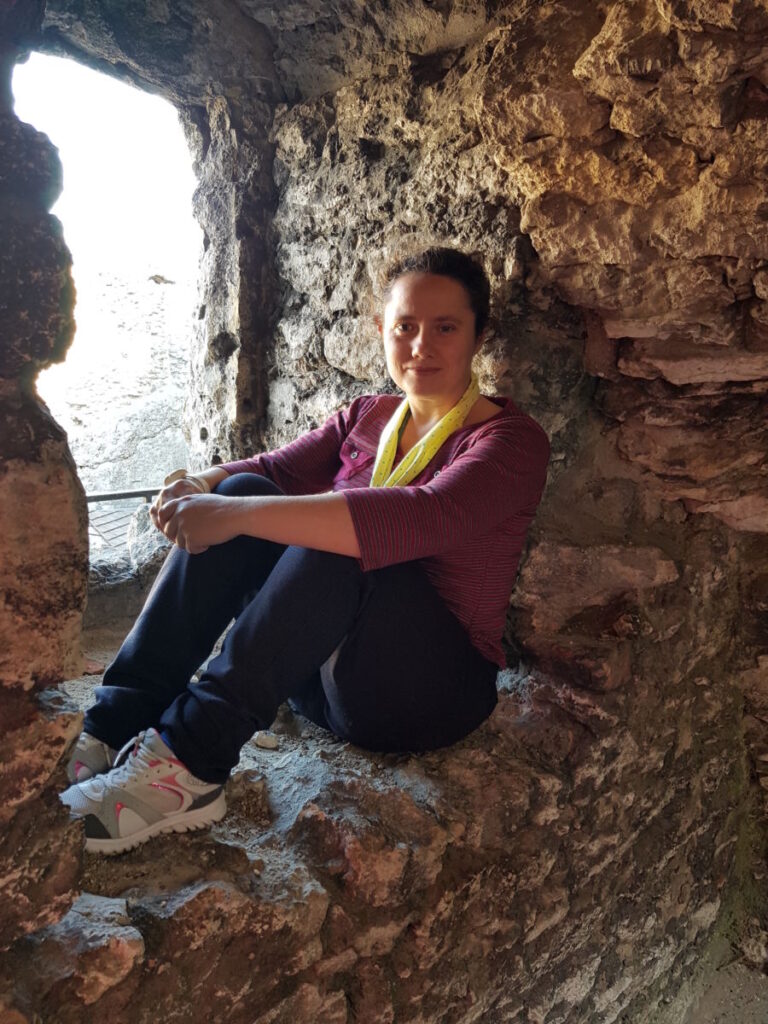 Uśmiechnięta mieszkanka siedząca bokiem i oparta placami o ścianę niszy okiennej w ruinach zamku