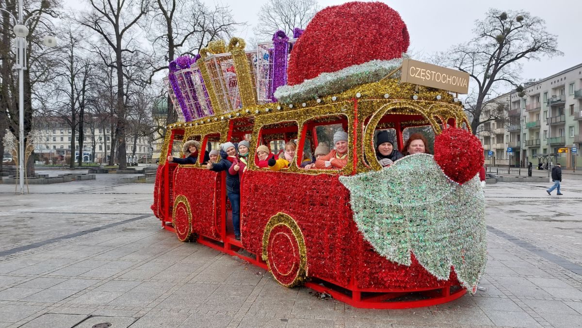Uśmiechnięte mieszkanki stojąc pozują w świątecznym autobusie, w tle plac i budynki częstochowski
