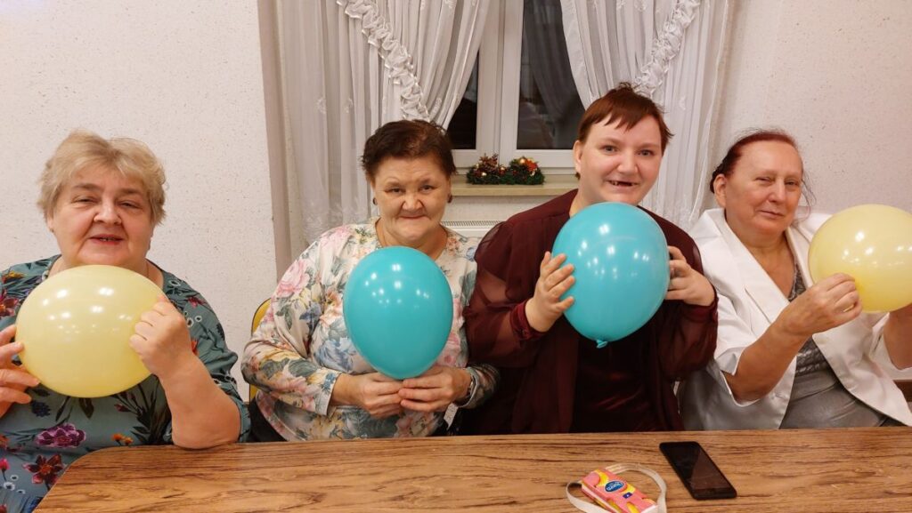 Cztery roześmiane mieszkanki siedzą przy stole z balonami w rękach