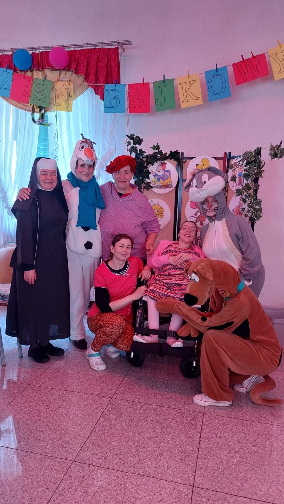 Na wspólnym zdjęciu na sali integracyjno zabawowej mieszkanki, siostra Albertynka oraz opiekunki przebrane za postaci z kreskówek - Olafa z Krainy Lodu, Scooby - Doo oraz Królika Bugsa. 