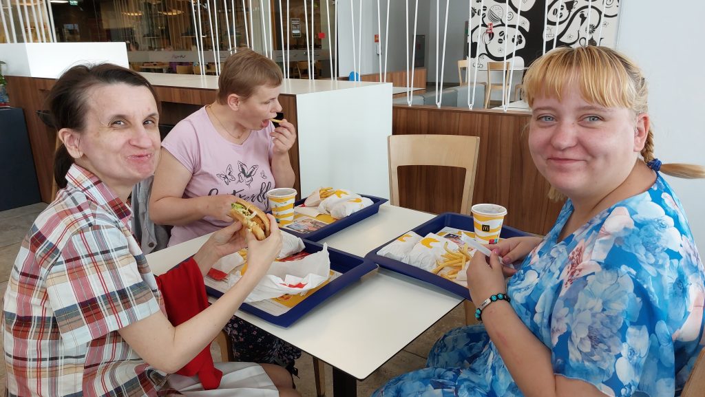 Trzy mieszkanki siedzące przy stole i jedzące burgery i frytki z Mc Donald's.