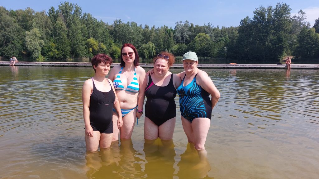 Uśmiechnięta grupa czterech mieszkanek stojąca w wodzie w kostiumach kąpielowych.