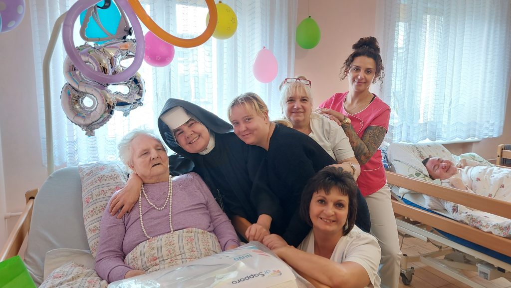 Wspólne zdjęcie Siostry Albertynki wraz z opiekunkami przy łóżku Mieszkanki.