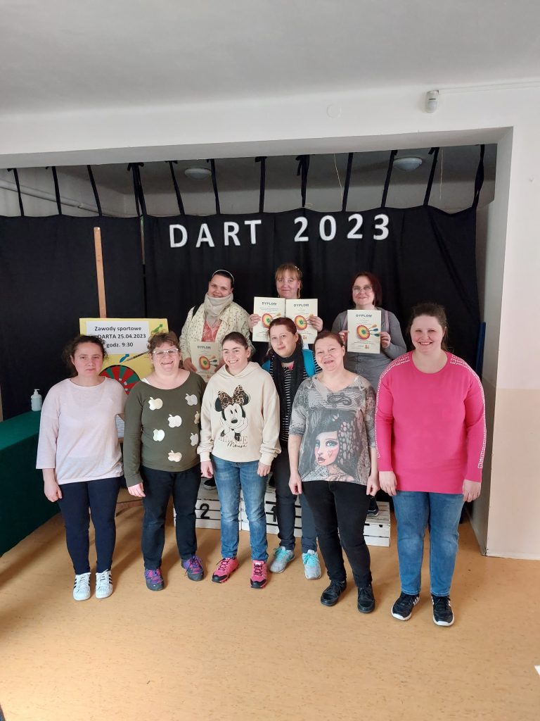 Grupa uśmiechniętych mieszkanek stoi w dwóch rzędach na tle napisu DART 2023. Mieszkanki stojące w drugim rzędzie na podium mają w rękach dyplomy