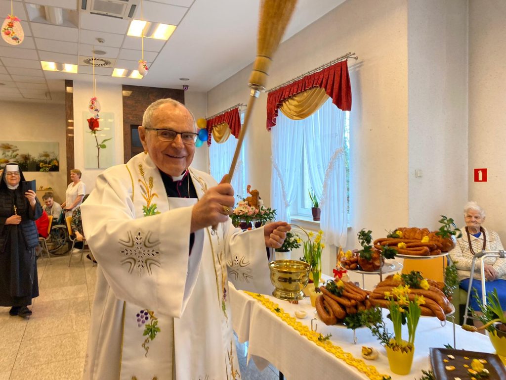 Uśmiechnięty ksiądz biskup podczas święcenia pokarmów na sali integracyjno - terapeutycznej