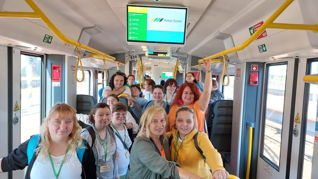 Roześmiany zespół Michalinki wraz z osobami odpowiedzialnymi za grupę pozuje do zdjęcia w wagonie kolejowym