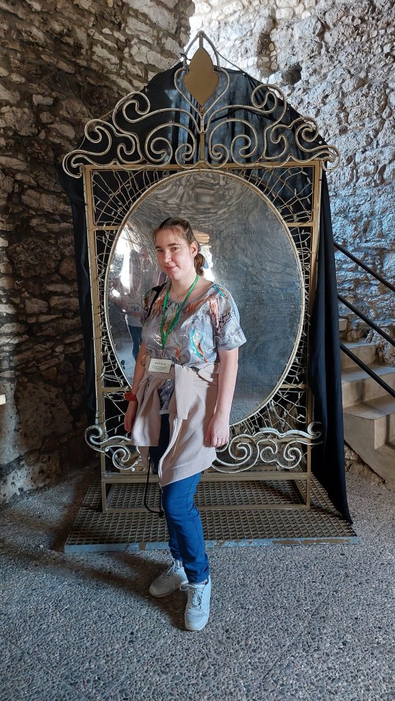 Uśmiechnięta mieszkanka pozuje do zdjęcia stojąc na tle lustra w korytarzu zamku