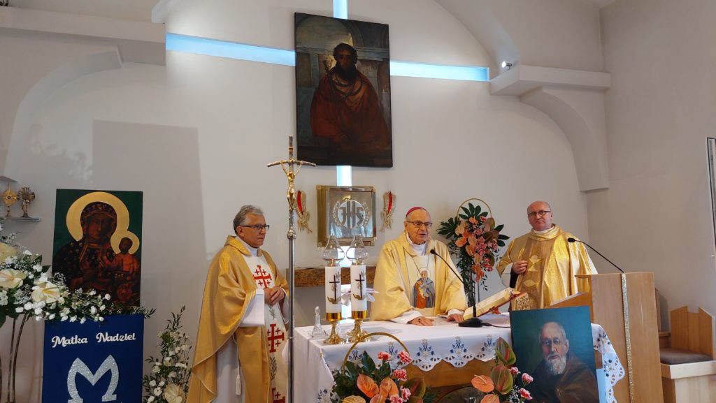 Trzech księży, w środku kapelan Domu, stoi przy ołtarzu w kaplicy, w tle obraz Chrystusa Ecce Homo, obok obraz Maryi. Przed ołtarzem obraz świętego Brata Alberta. 