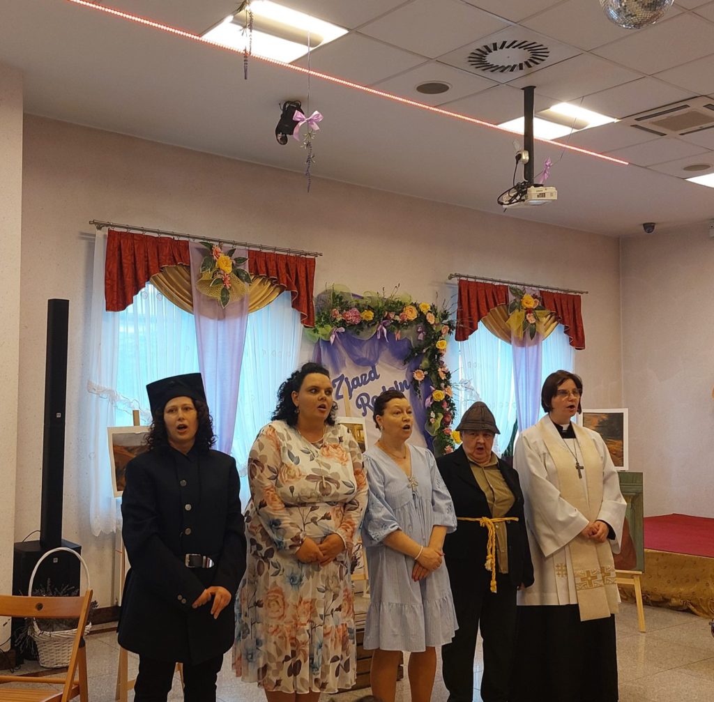 Pięć mieszkanek stoi i śpiewa podczas występu artystycznego na sali integracyjno - terapeutycznej. trzy z nich przebrane są za żołnierza, żebraka i księdza.