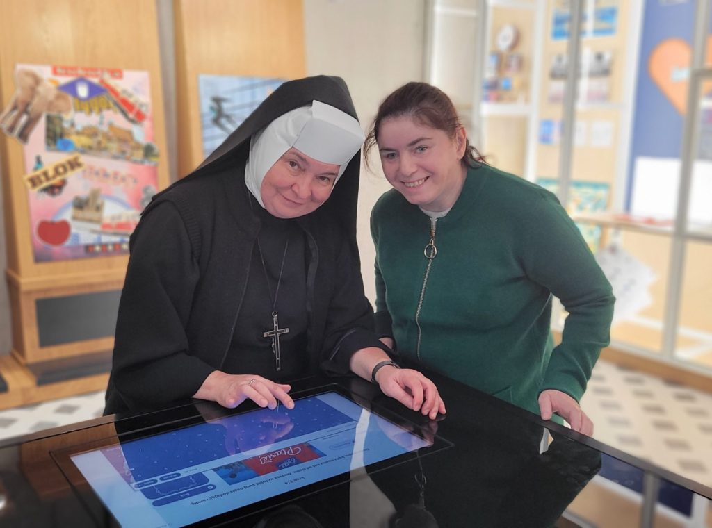 Uśmiechnięte siostra Albertynka wraz z mieszkanką stojąc pozują do zdjęcia przy multimedialnym stole z aplikacją do projektowania