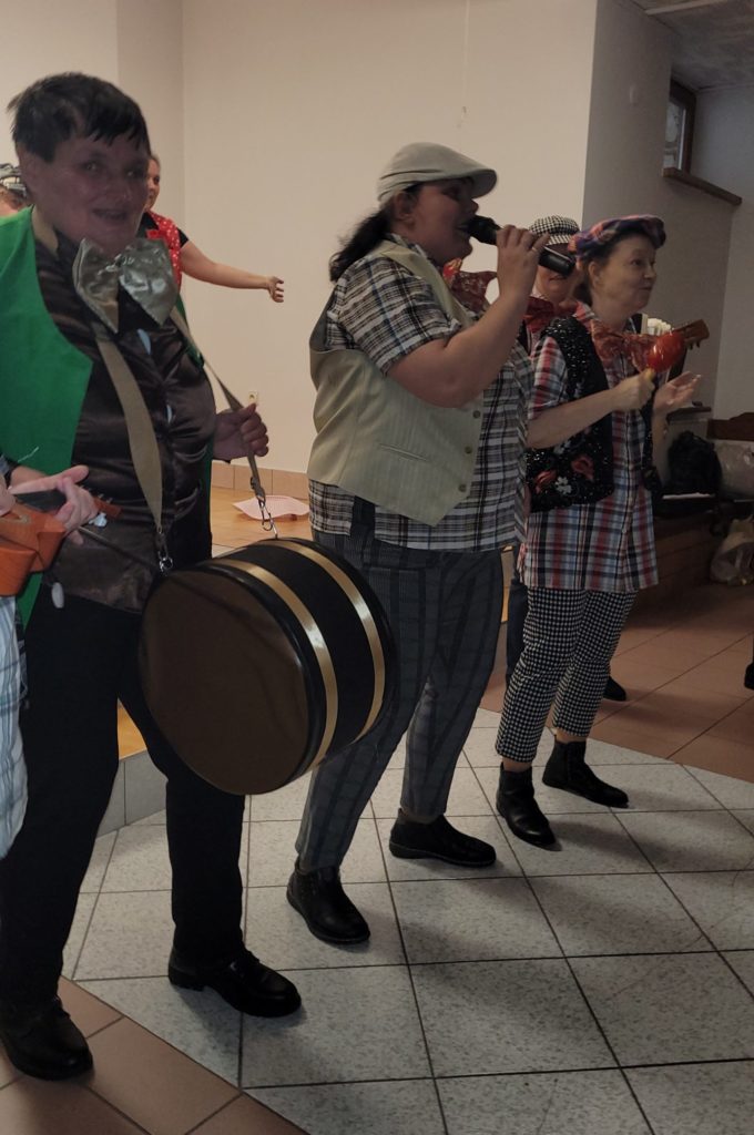 Mieszkanki na scenie podczas występu biesiadnego. Dwie z nich mają w rękach instrumenty, osoba pomiędzy nimi śpiewa.