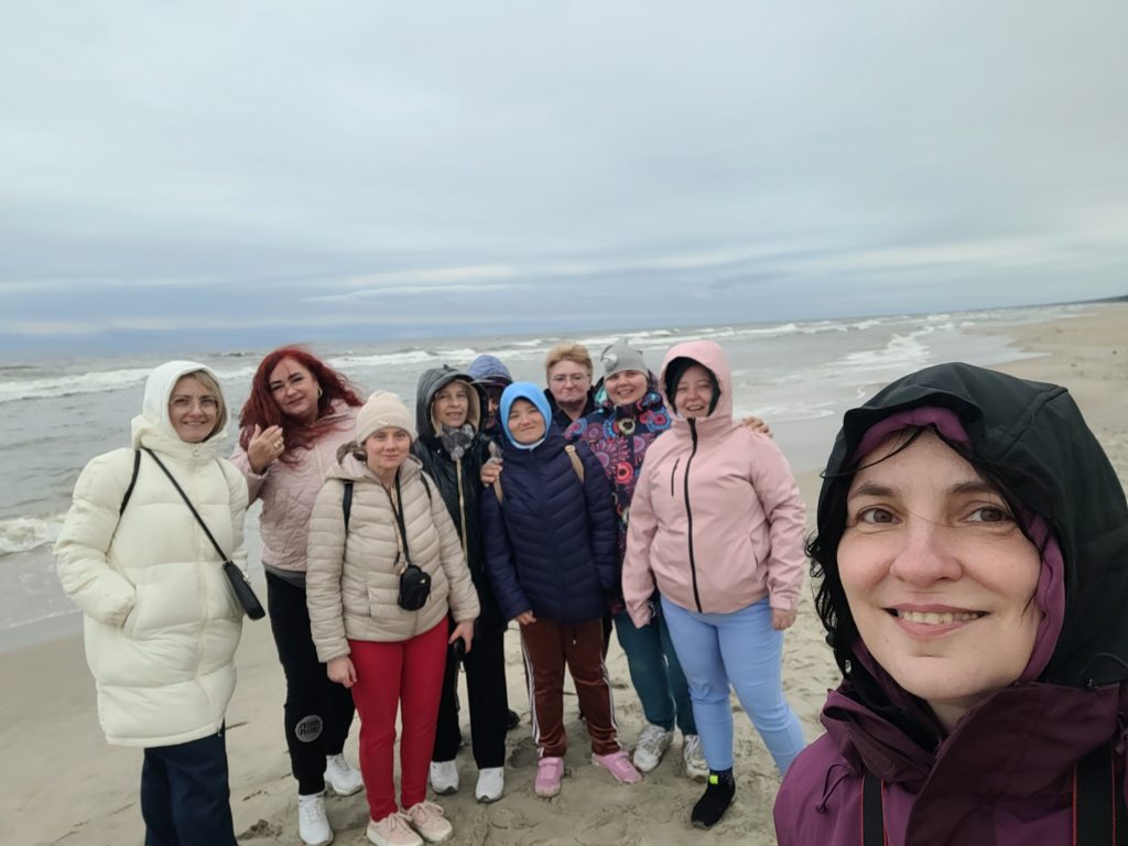 Zdjęcie selfie stojącej na tle morza małej grupy roześmianych mieszkanek wraz z ich opiekunkami na wycieczce