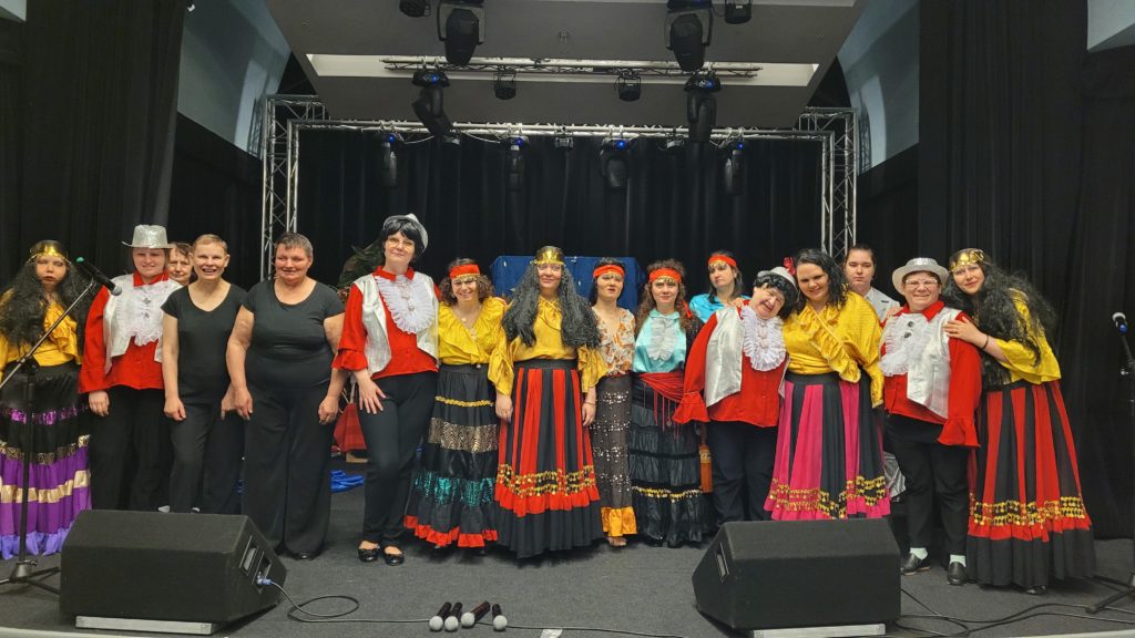 Grupa roześmianych mieszkanek z zespołu Michalinki stojąc pozuje do zdjęcia przed występem. Wszyscy są w strojach scenicznych
